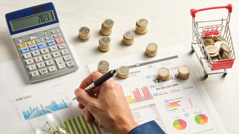 mano che scrive, carrello spesa, soldi e calcolatrice